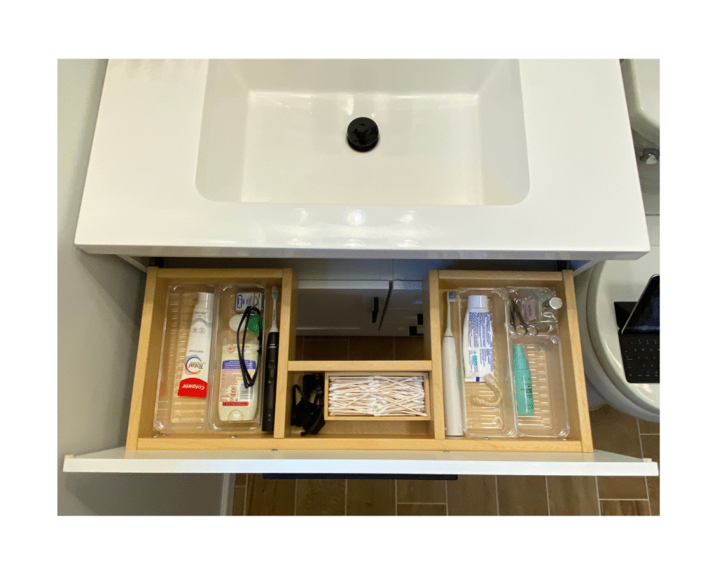 Top-down view of small bathroom remodel storage using clear acrylic dividers inside a custom u-shaped vanity drawer.